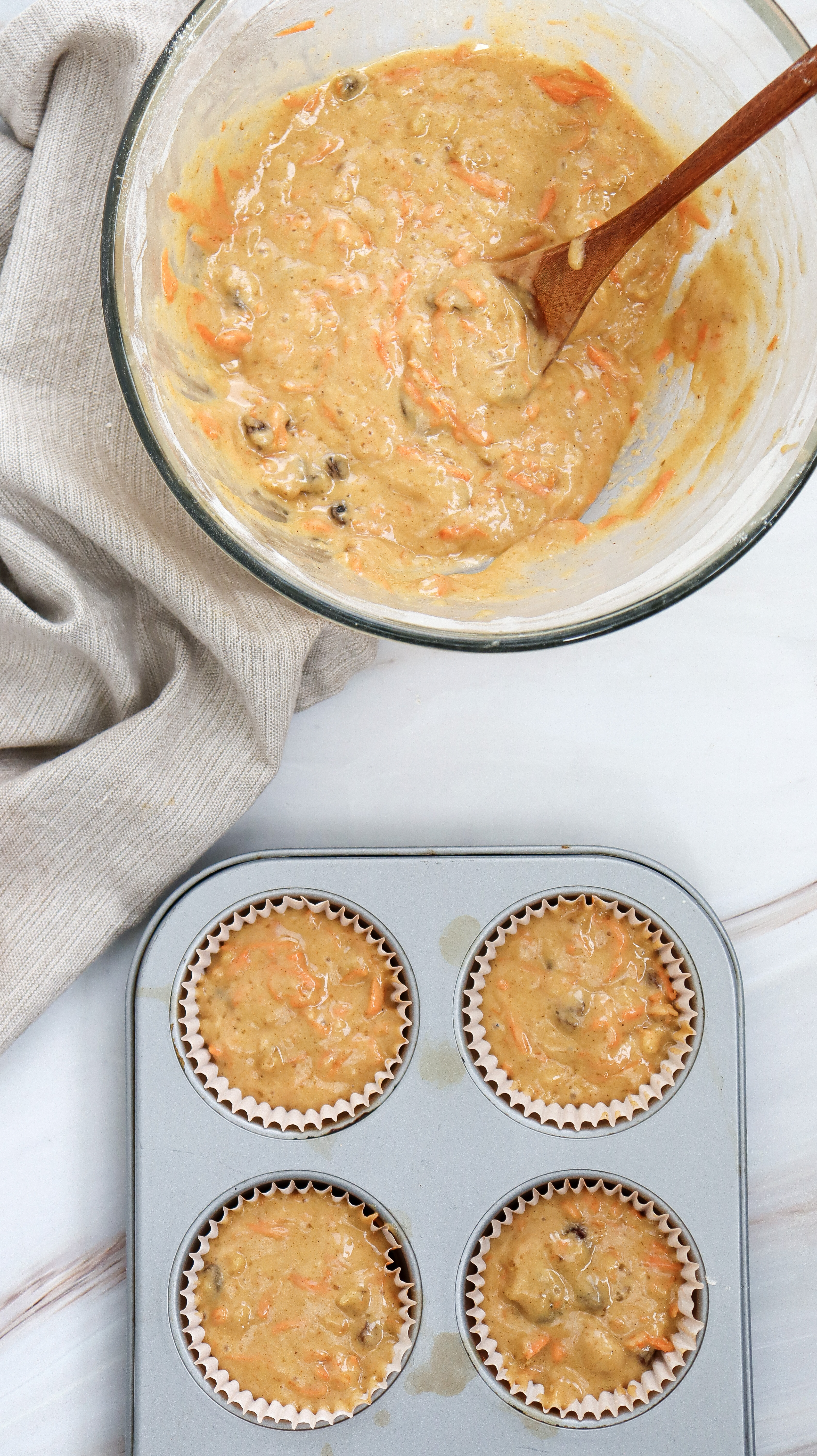 A muffin tin with each cavity filled with carrot cake muffin batter, set on a countertop.
