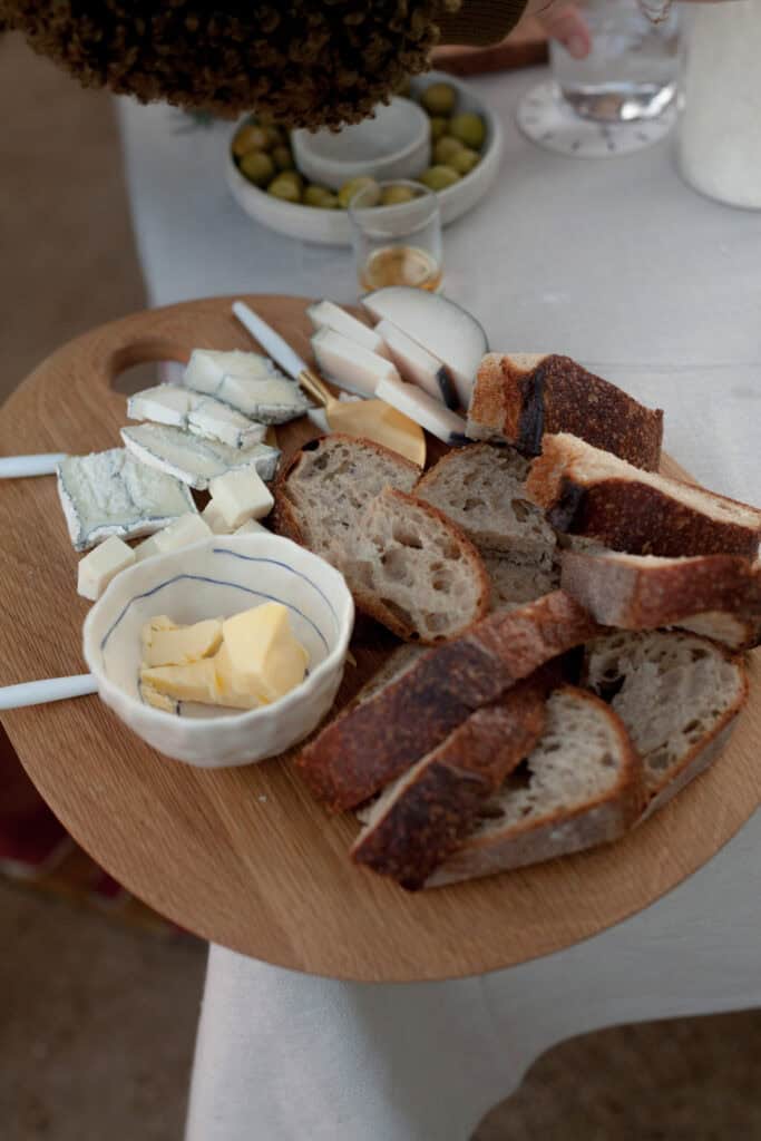 A rustic wooden board with an assortment of cheeses, fresh bread slices, and a small dish of honey, perfect for entertaining.