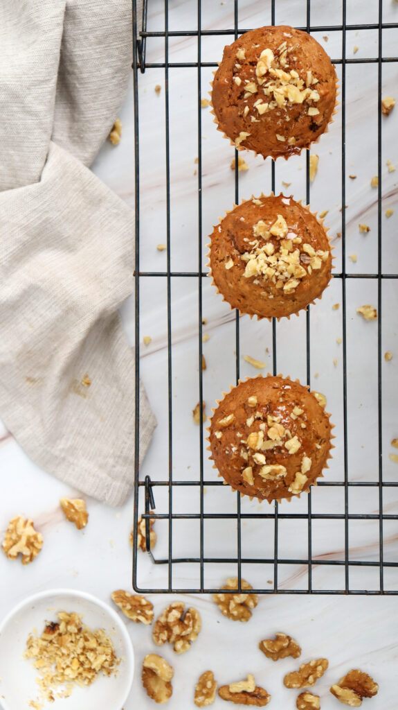 A close-up of golden-brown carrot cake muffins resting on a wire cooling rack, with a rustic kitchen towel in the background.