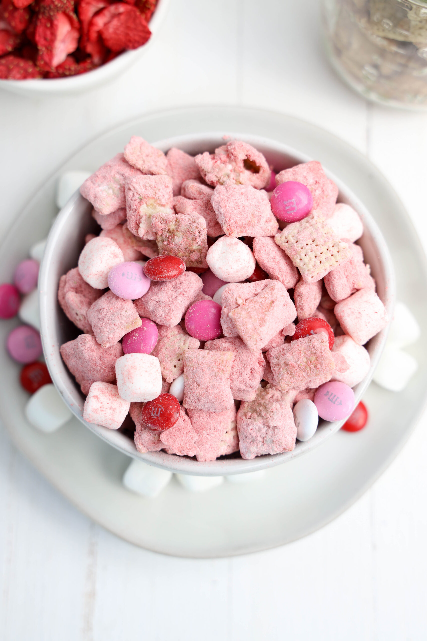 A bowl of Strawberry Puppy Chow with Chex cereal, powdered strawberry coating, M&Ms, and marshmallows.