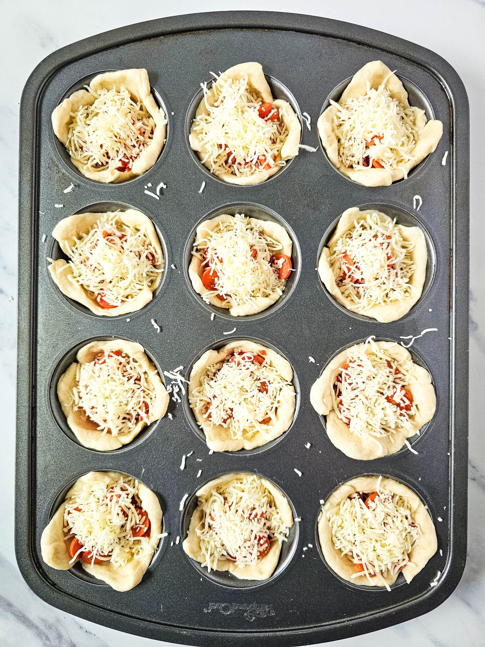 Process of making pepperoni pizza puffs: dough squares placed in a muffin pan, filled with cheese, sauce, and pepperoni before baking.