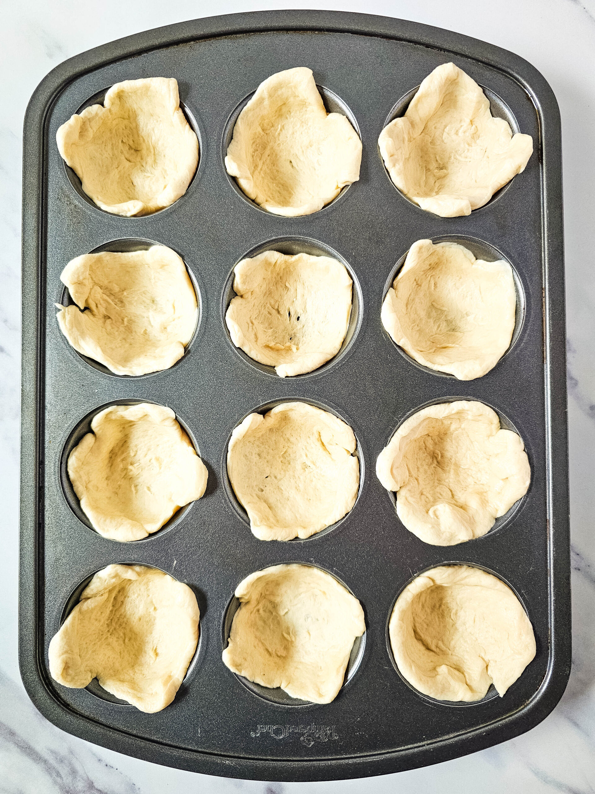 Prepped muffin tin with pizza dough cups for making pepperoni pizza puffs.