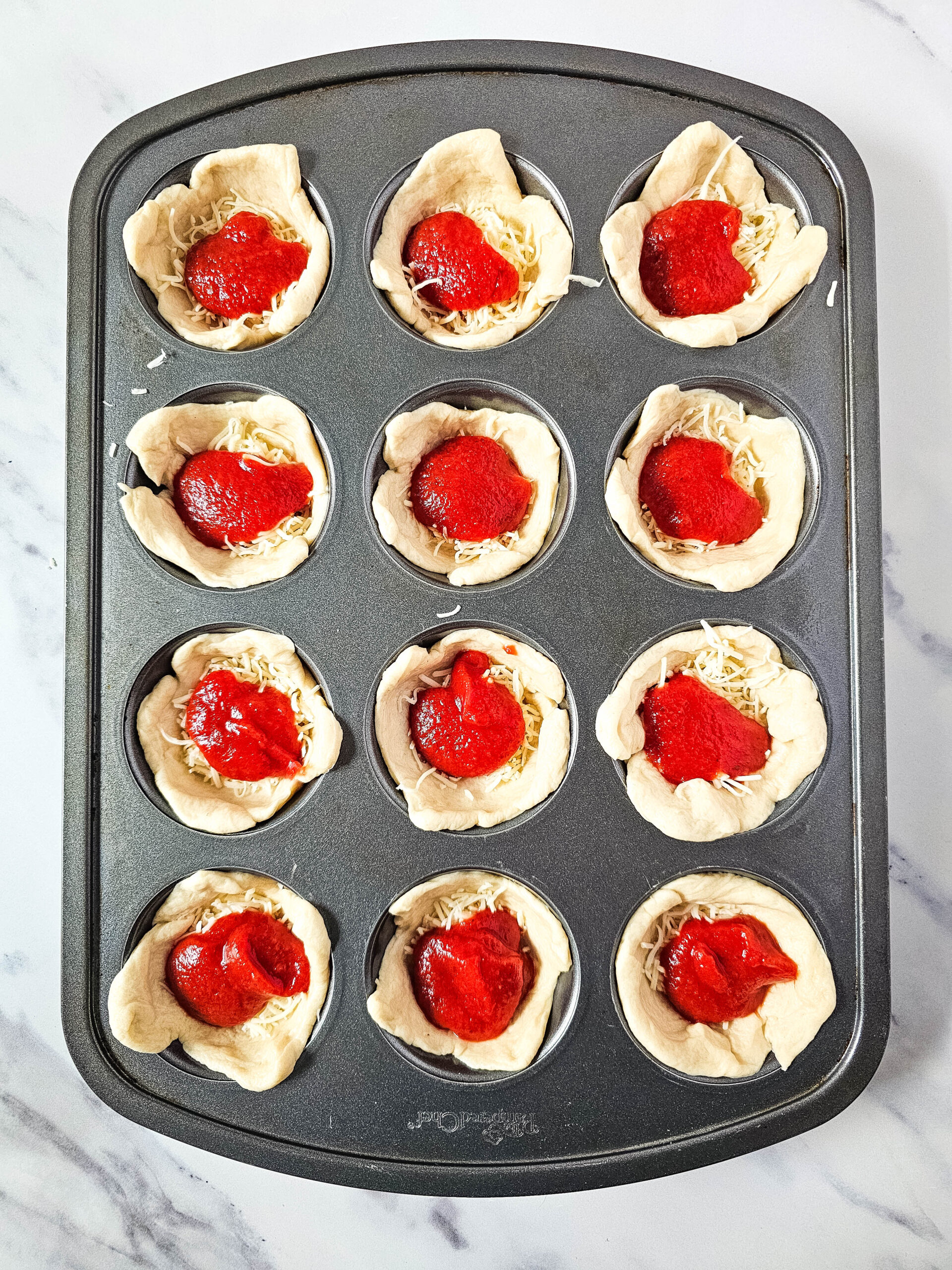 Assembling pepperoni pizza puffs by layering mozzarella, pizza sauce, and mini pepperoni in dough cups inside a muffin pan