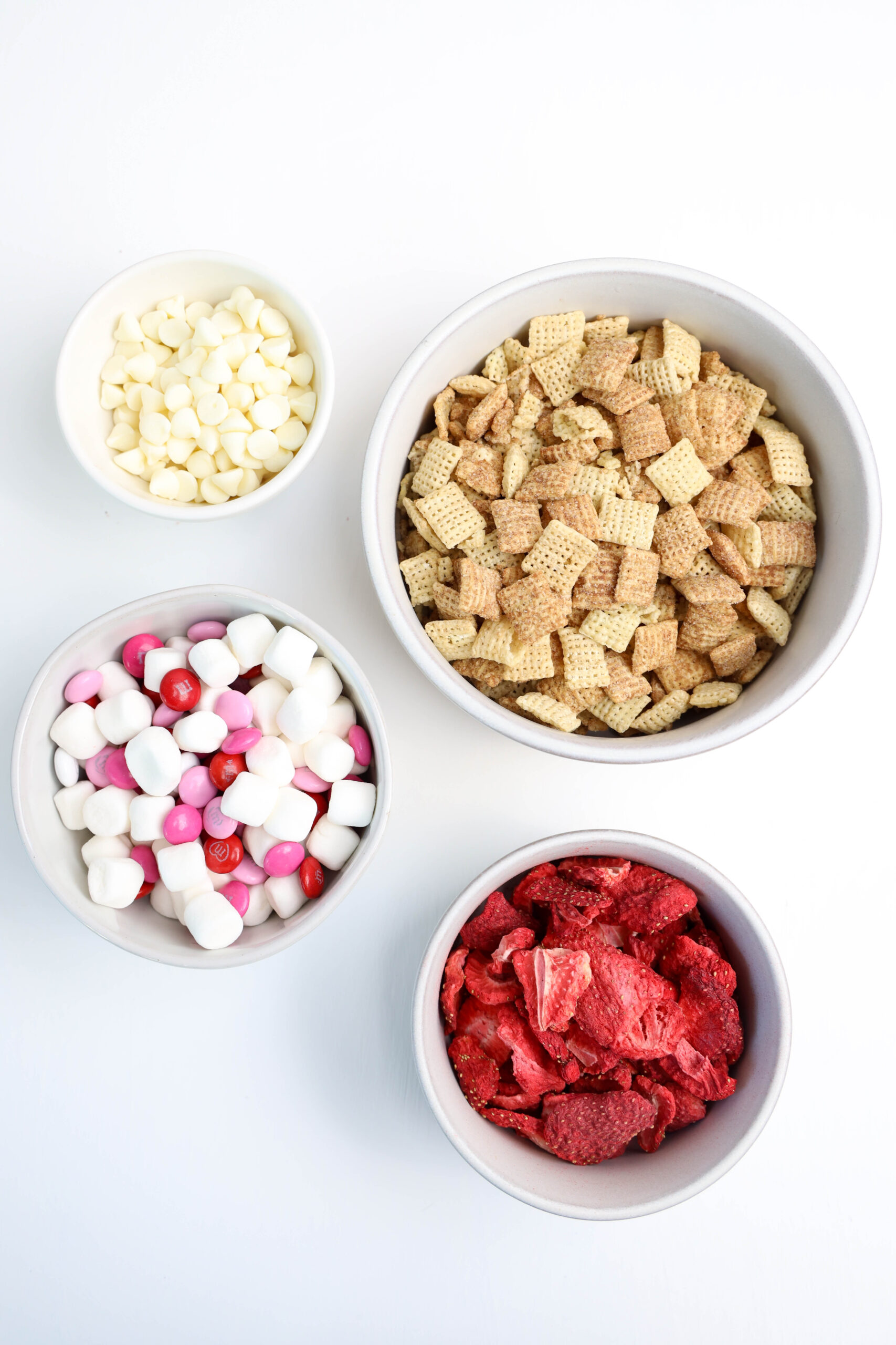Ingredients for Strawberry Puppy Chow, including cinnamon Chex cereal, white chocolate chips, freeze-dried strawberries, powdered sugar, Valentine’s M&Ms, and marshmallows.