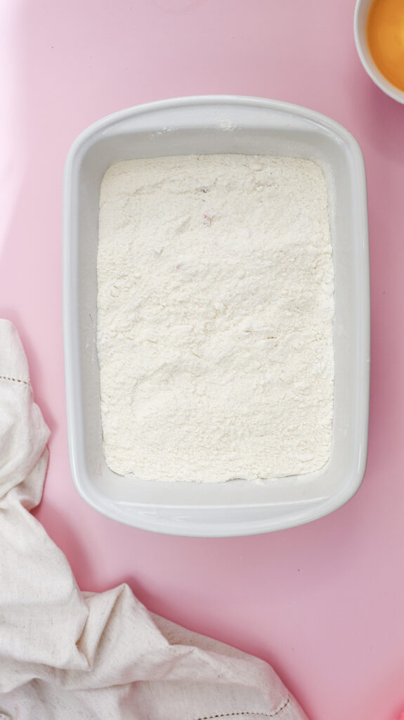 Overhead shot of yellow cake mix being sprinkled over cherry pie filling in a white baking dish.