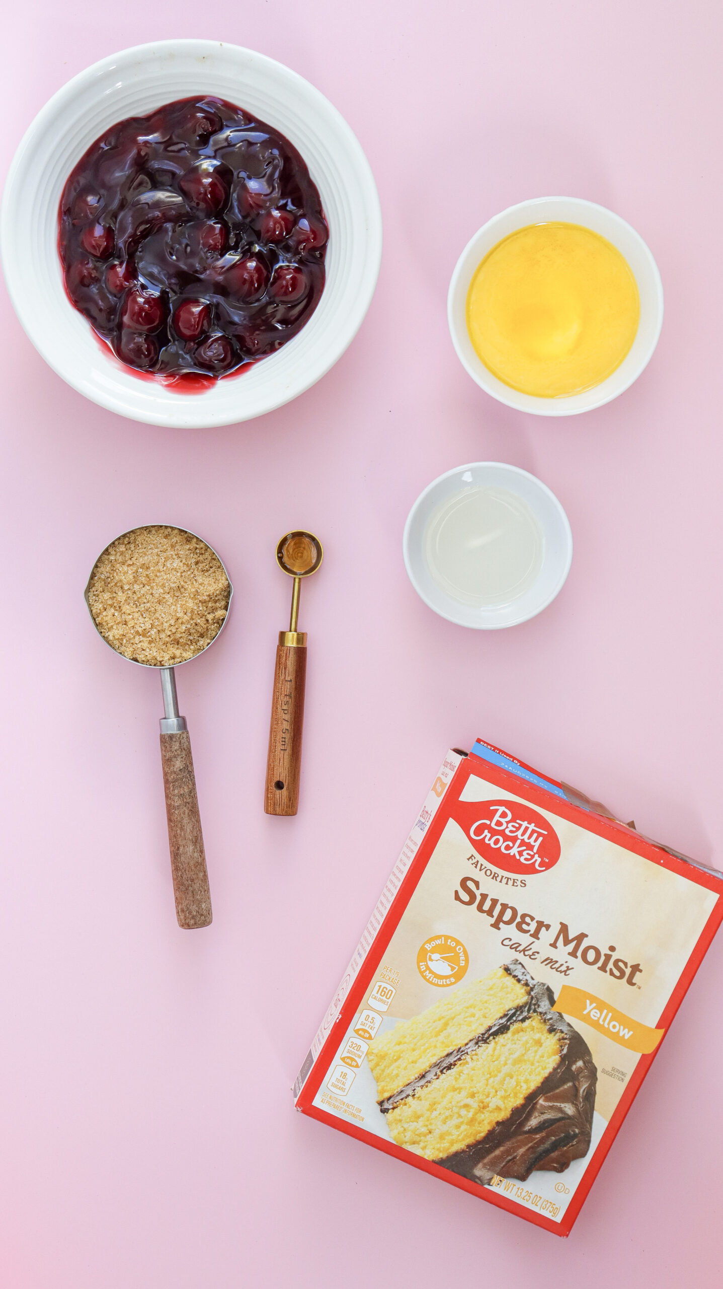 Overhead shot of ingredients for Cherry Dump Cake, including canned cherry pie filling, yellow cake mix, and butter on a marble countertop.
