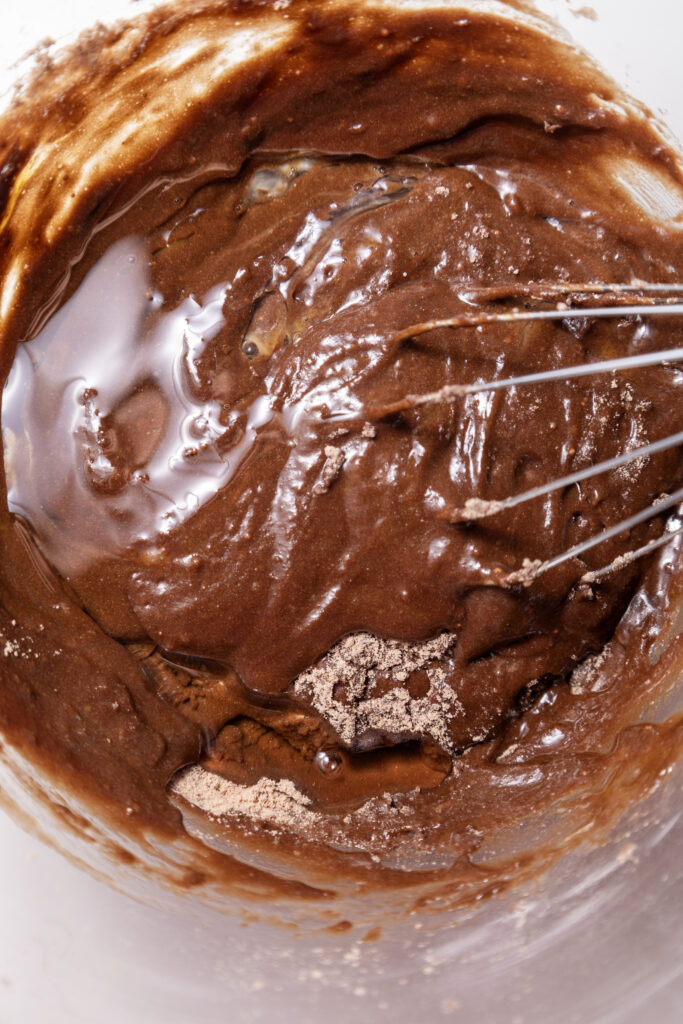 Thick and glossy chocolate brownie batter being stirred in a mixing bowl.