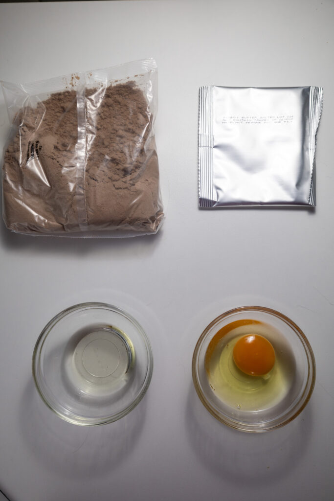 All the ingredients for a peanut butter brownie recipe, including chocolate, peanut butter, eggs, flour, and sugar.