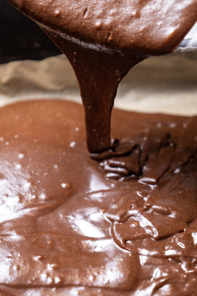 Smooth chocolate brownie batter being poured into a lined baking pan.