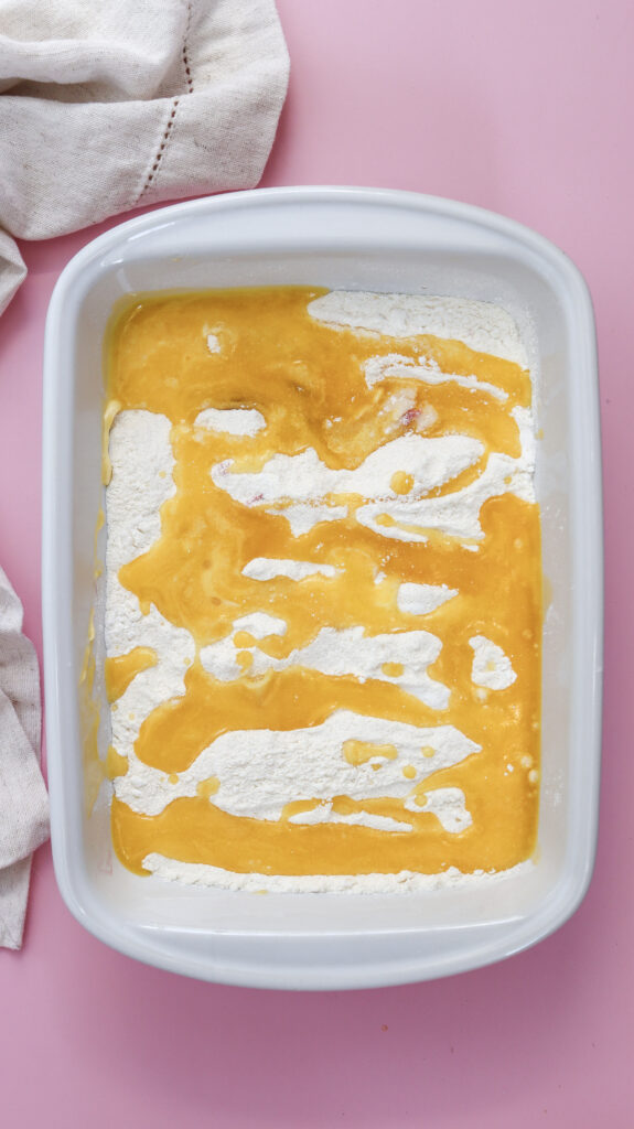 Melted butter drizzled on top of cake mix in a white baking dish before baking.